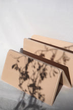 A beige foldable card case with a printed botanical shadow pattern, shown partially open on a light gray surface with dappled shadows cast across it. The brand name 'muno' is printed on the front.