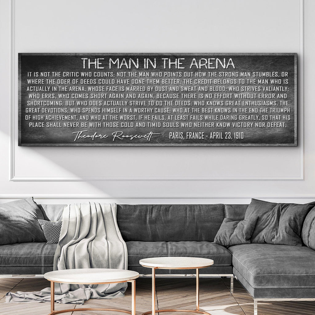 Framed black and white quote by Theodore Roosevelt on a wall above a gray sofa.
