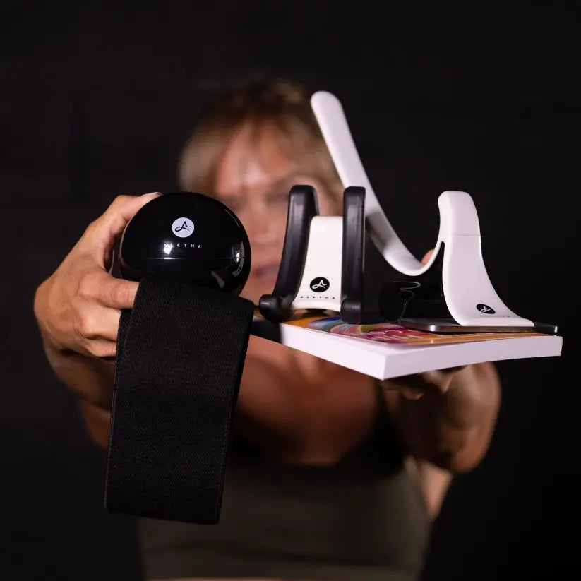 Person holding a black ball and white exercise equipment against a dark background