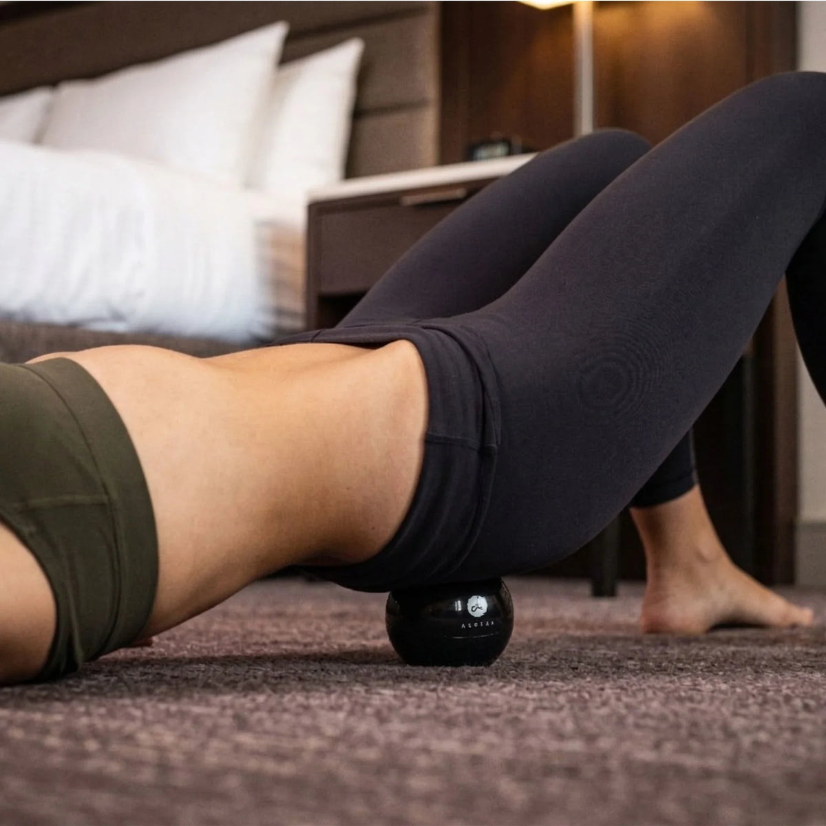 Person using a black massage ball on their leg in a bedroom setting