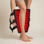Person using a red light therapy device on their leg against a neutral background