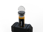 A cylindrical battery with a black and yellow Fenix label is shown inserted into a black device, with a clear circular cover or lens propped open above the battery on a white background.