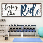 Gym interior with weight rack and motivational sign 'Enjoy the Ride'.