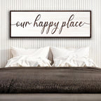 Framed artwork with 'our happy place' text above a bed in a bedroom setting.