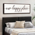 Bedroom with a large framed sign above the bed reading 'our happy place'.