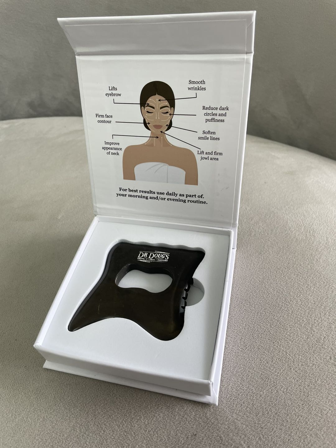 Black facial tool in a white box with an illustration of a woman's face on a gray surface